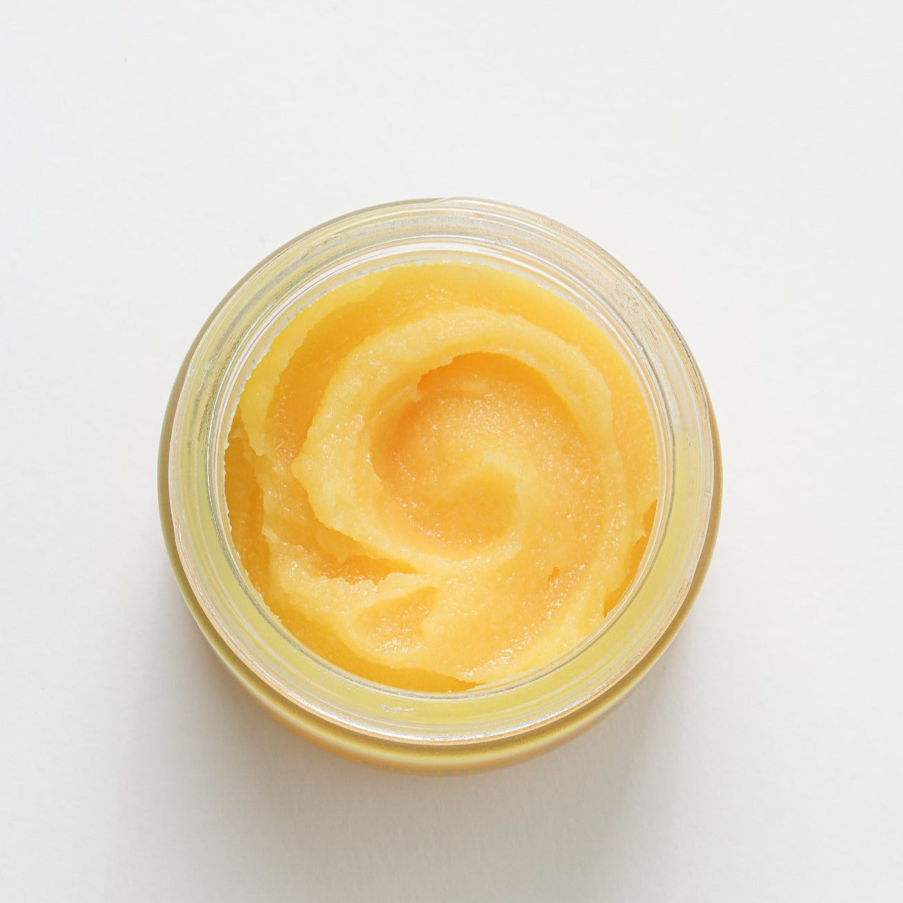 The image shows an open jar filled with a thick, orange exfoliating skincare product. The jar is viewed from above against a white background. 